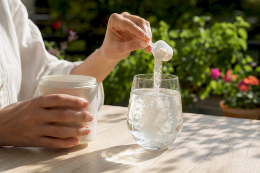 Des mains ouvrent un flacon de complément alimentaire au collagène, laissant apparaître de la poudre blanche, posée à côté de quelques coquillages.